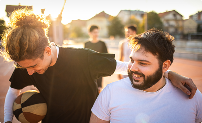 Men laughing outdoors, one holding a basketball